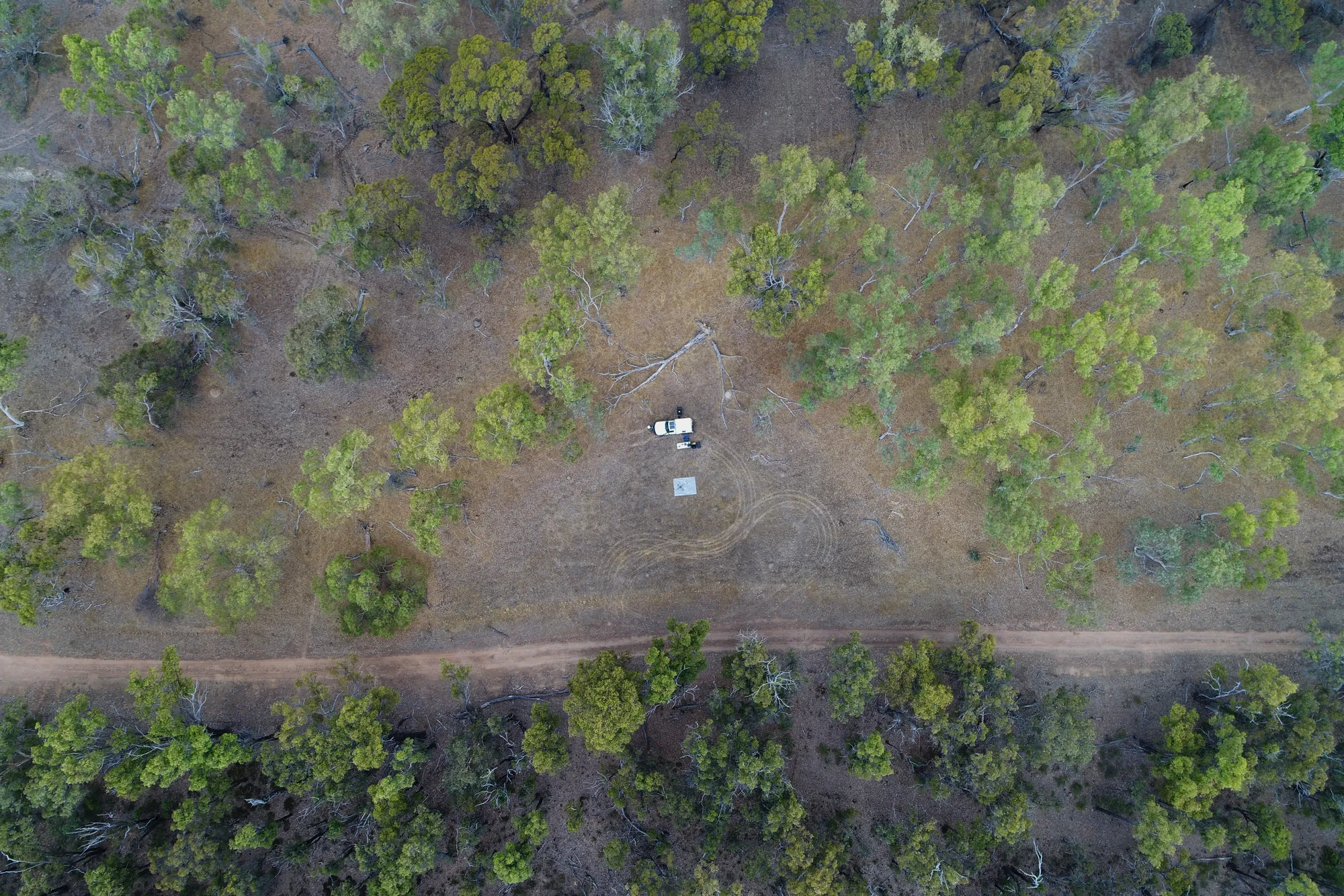 Aerial view over remote bushland during a drone survey, vehicle and launch pad among the trees
